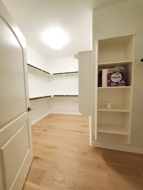 Finished walk-in closet with built-in shelving, hanging rails, and new flooring